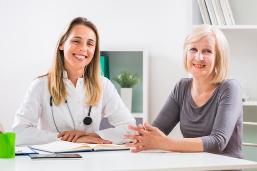 Portrait of female doctor and senior woman patient sitting in doctor's office