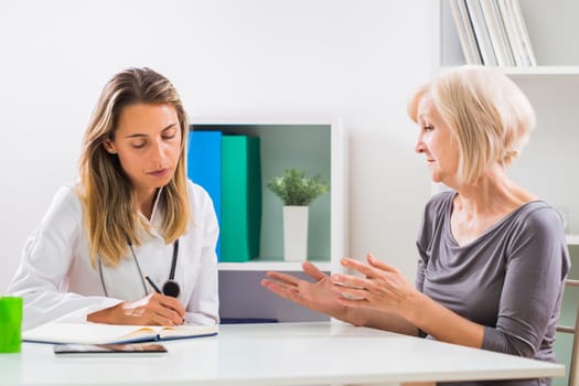 Female doctor and senior woman patient talking in doctor's office.