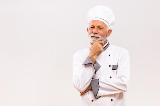 Portrait of senior chef thinking  on gray background.