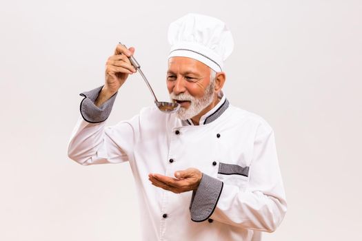 Portrait of content senior chef tasting soup.