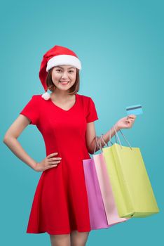 Santa asian woman holding shopping bags and credit card against blue vignette