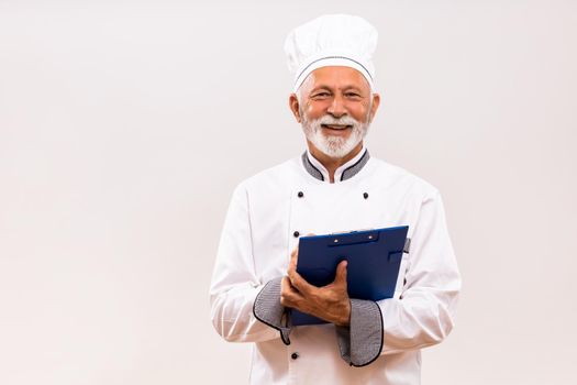 Portrait of senior  chef holding cookbook on gray background.