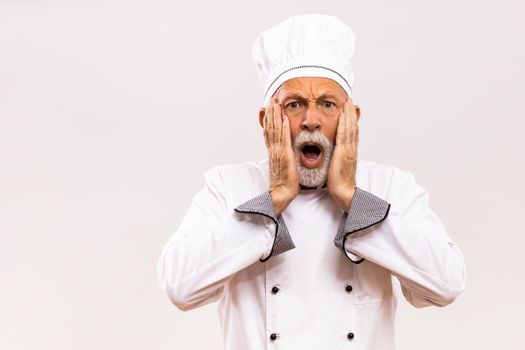 Portrait of  shocked senior chef on gray background.