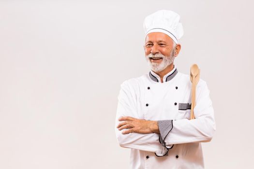 Portrait of  senior chef with work tool on gray background.