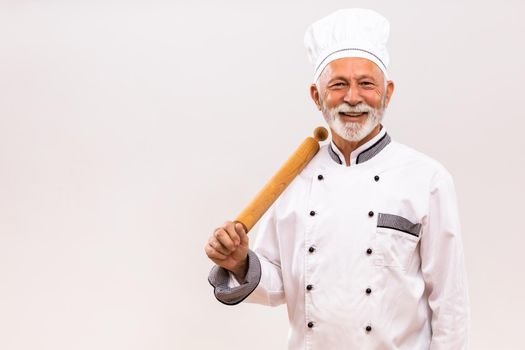 Portrait of senior chef with rolling pin on gray background.