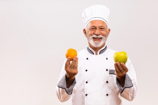 Portrait of senior chef shows fruit on gray background.