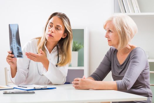 Female doctor is showing x-ray image to her senior woman patient in doctor office.