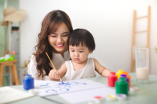 Happy family mother and daughter together paint. Asian woman helps her child girl.