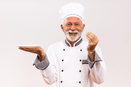 Image of  senior chef with empty plate  showing delicious sign on gray background.