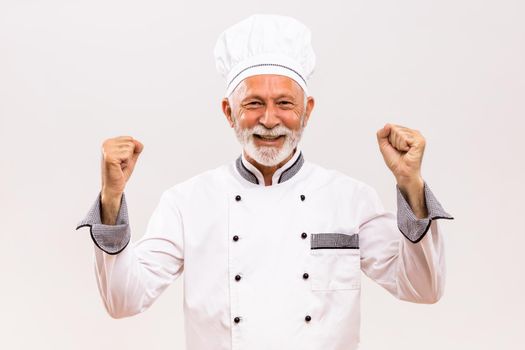 Portrait of  excited senior chef on gray background.