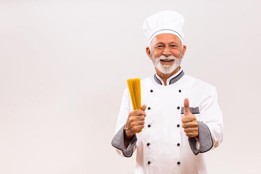 Portrait of senior chef holding spaghetti and showing thumb up  on gray background.