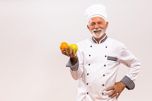 Image of senior chef holding  fruit and thinking on gray background.