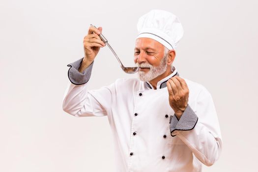 Portrait of content senior chef tasting soup