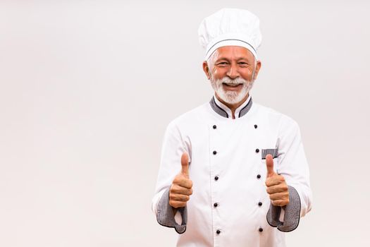 Portrait of  senior chef showing thumb up on gray background.