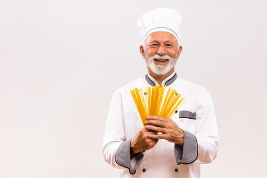 Portrait of senior chef holding spaghetti on gray background.