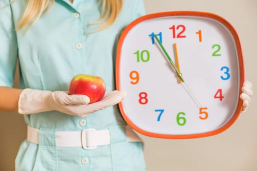 Image of medical nurse doctor holding apple and clock.Focus on apple.
