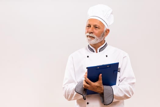 Portrait of senior  chef holding cookbook on gray background.