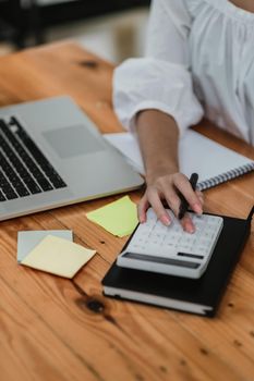 Close up hand of accountant or bookkeeper using calculator calculating financial expense at home office.