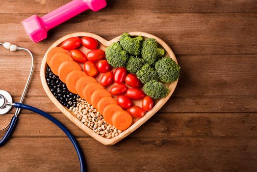 Top view of fresh organic fruits and vegetables in heart plate wood (carrot, Broccoli, tomato), doctor stethoscope and sport dumbbell on wooden table, Healthy lifestyle diet food concept