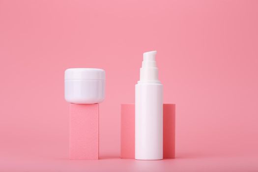 Modern trendy set of two white cosmetic jars on pink geometric shapes for product presentation against pink background. Minimal concept of skin care creams for face and under eye area or lips