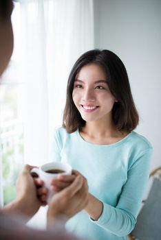 Beautiful young couple is smiling while drinking tea in kitchen at home