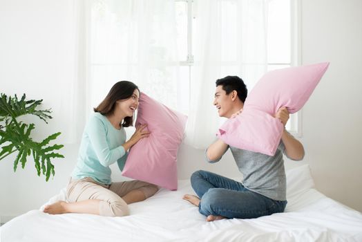 Happy asian couple having pillow fight in bed at home. Family fun concept.
