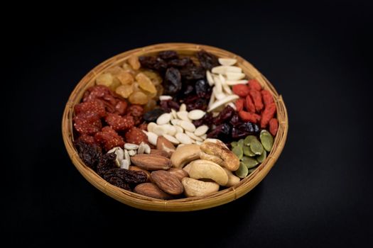 Group of various types of whole grains and dried fruits on a bamboo tray on black background.