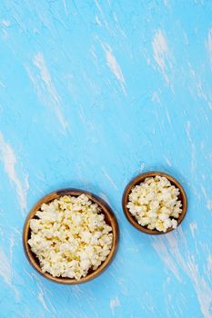 bowls of popcorn in small and large portions on a blue background. The concept of leisure and entertainment. Vertical photo