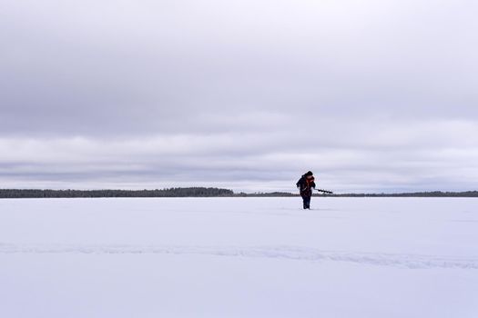 man drills holes for ice fishing with an electric auger. selective focus