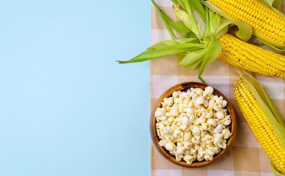 Corn on the cob, popcorn on a blue background. Topic - agro, corn cultivation, harvest. Copyspace