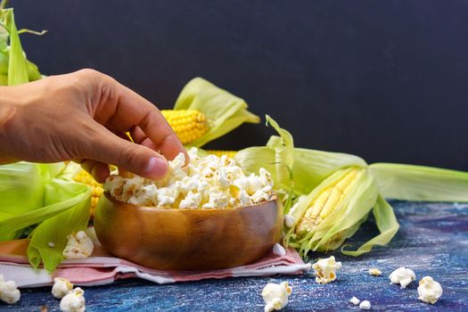 A bowl of popcorn with cobs of fresh corn on a dark background. Leisure.