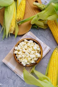 Homemade popcorn served in bowl together with raw corns. On a gray concrete table. Vertical photo