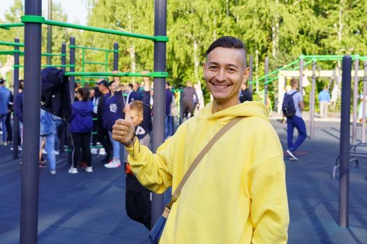 A young cheerful man in a yellow jacket on the background of a sports field. Selective focus