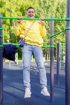 A young man in a yellow jacket pulls himself up on a horizontal bar. Selective focus. Sports event