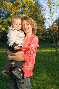 Happy mother holding her baby boy in the autumn park