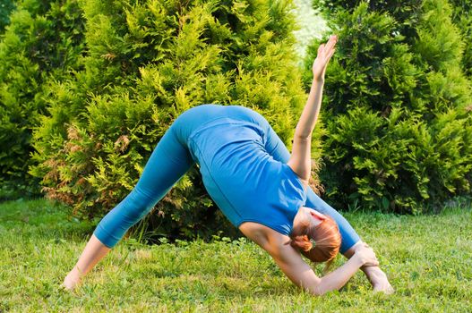 Beautiful red woman doing fitness or yoga exercises outdoors in a green park