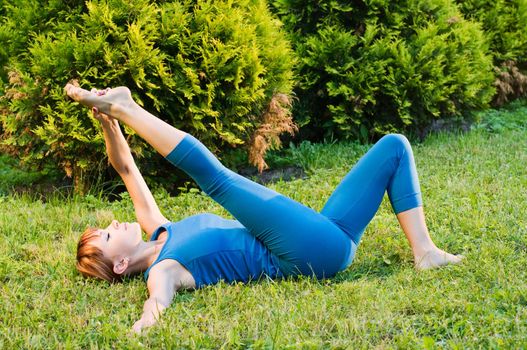 Beautiful red woman doing fitness or yoga exercises outdoors in a green park