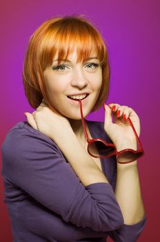 Portrait of beautiful red woman wearing heart-shaped sunglasses posing at the studio