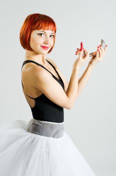Beautiful red girl performing makeup using lipstick and mirror