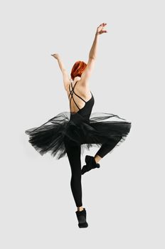 Beautiful ballerina wearing black tutu dancing on gray background