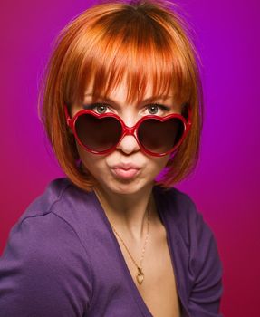 Portrait of beautiful red woman wearing heart-shaped sunglasses posing at the studio