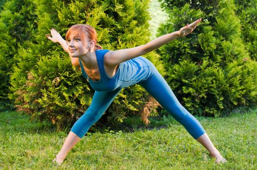 Beautiful red woman doing fitness or yoga exercises outdoors in a green park