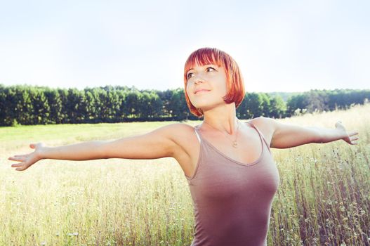 Happy red girl with outstretched hands outdoors in the field