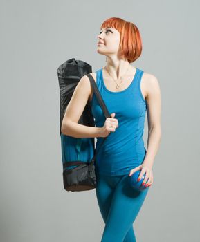 Red-haired fitness girl with yoga mat at the gym