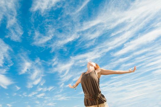 Beautiful young dancer performing yoga-dance outdoors with blue sky and clouds in the background