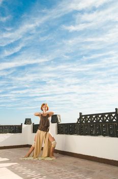 Beautiful young dancer performing yoga-dance outdoors with blue sky and clouds in the background