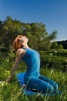 Beautiful red haired woman practicing fitness yoga outdoors on a summer day