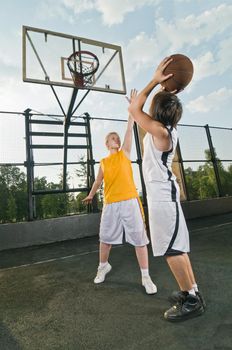 Two teenagers playing basketball at the street playground