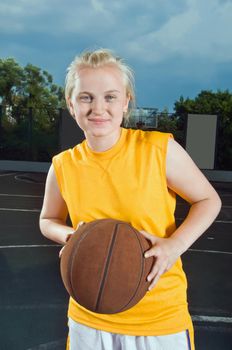 Teenage girl wearing yellow holding basketball at the street playground