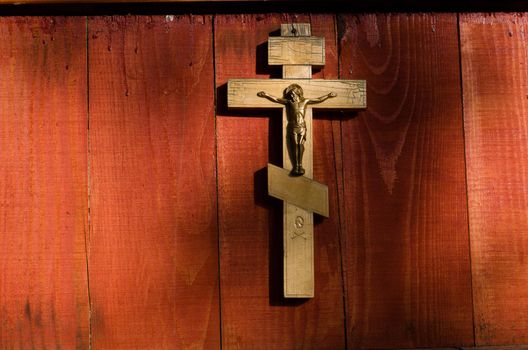 Small wooden crucifix hanging on wooden wall under beam of light